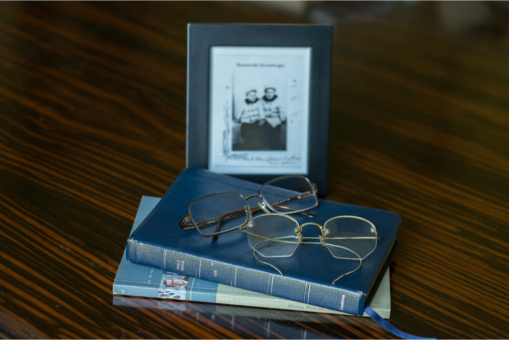 Two books stacked with glasses on top in front of a slightly blurry framed image.