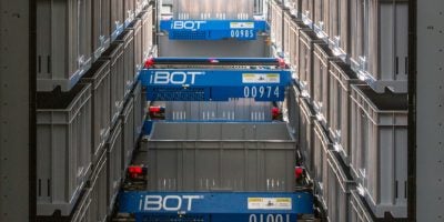 Three blue and silver Perfect Pick® robotic shuttles by OPEX®, part of an advanced automated storage and retrieval system (AS/RS), move in narrow aisles between stacked shelves in a warehouse.